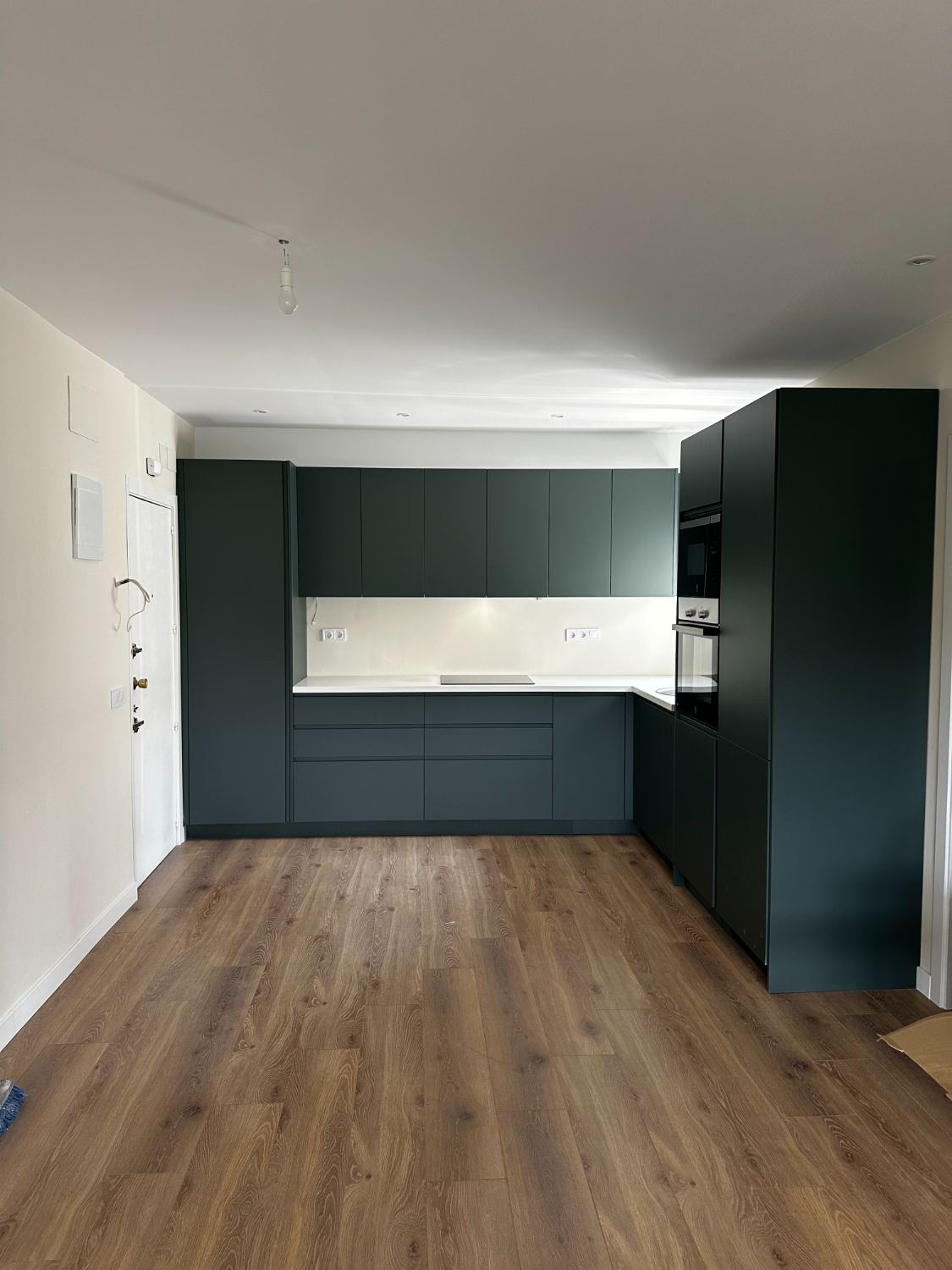 Cocina terminada en verde oscuro con encimera blanca y suelo de madera